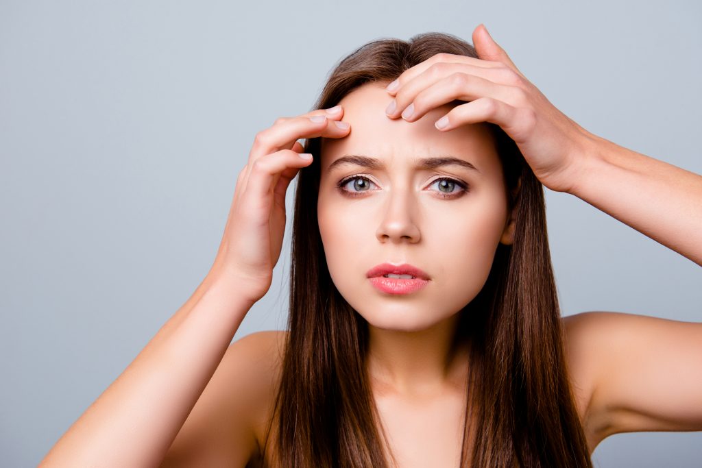 Young woman examining forehead.