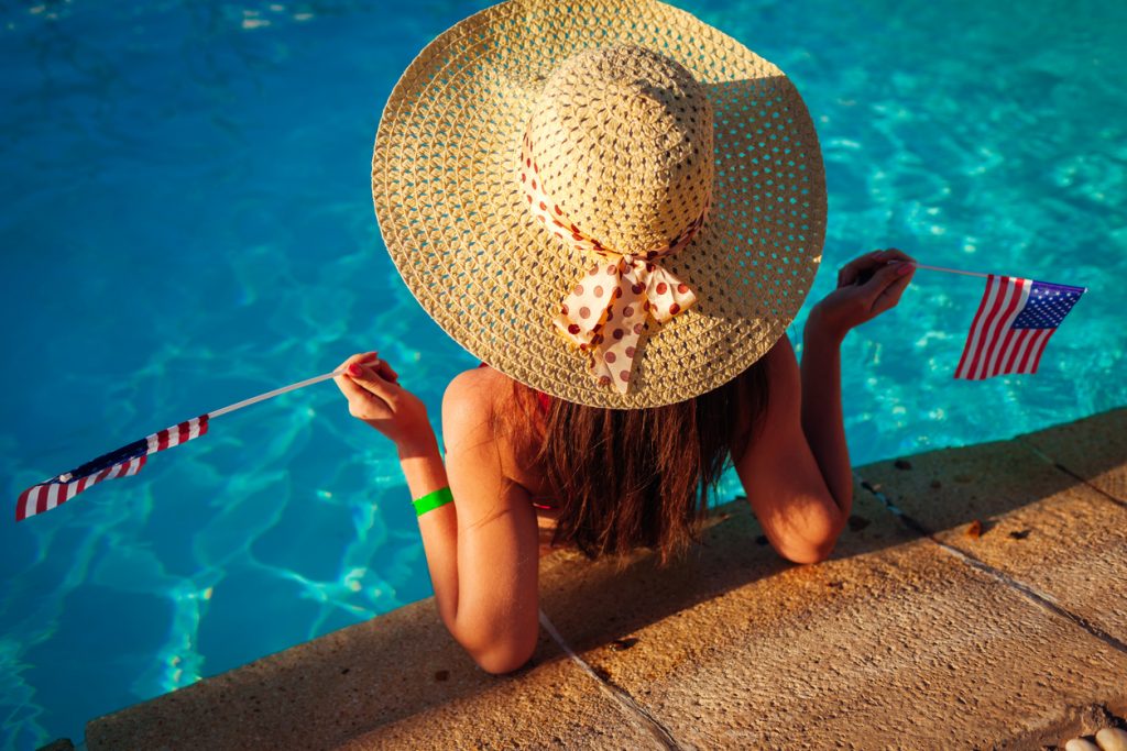 Woman in pool with large sun hat and flags.