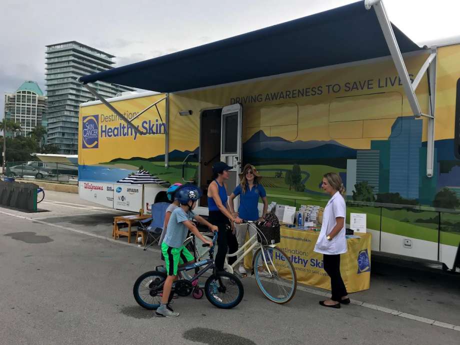 People on bikes in front of mobile healthy skin trailer.